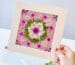 Hand holding framed pressed flower mandala made with seasonal pressed flower materials