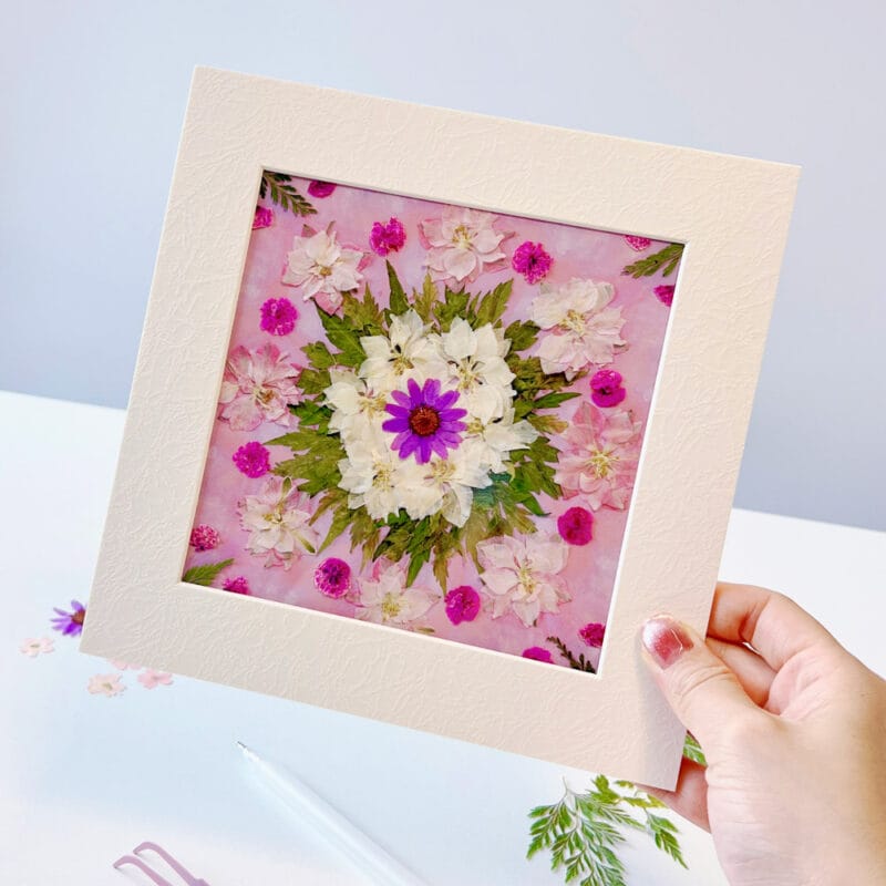 Hand holding framed pressed flower mandala made with seasonal pressed flower materials