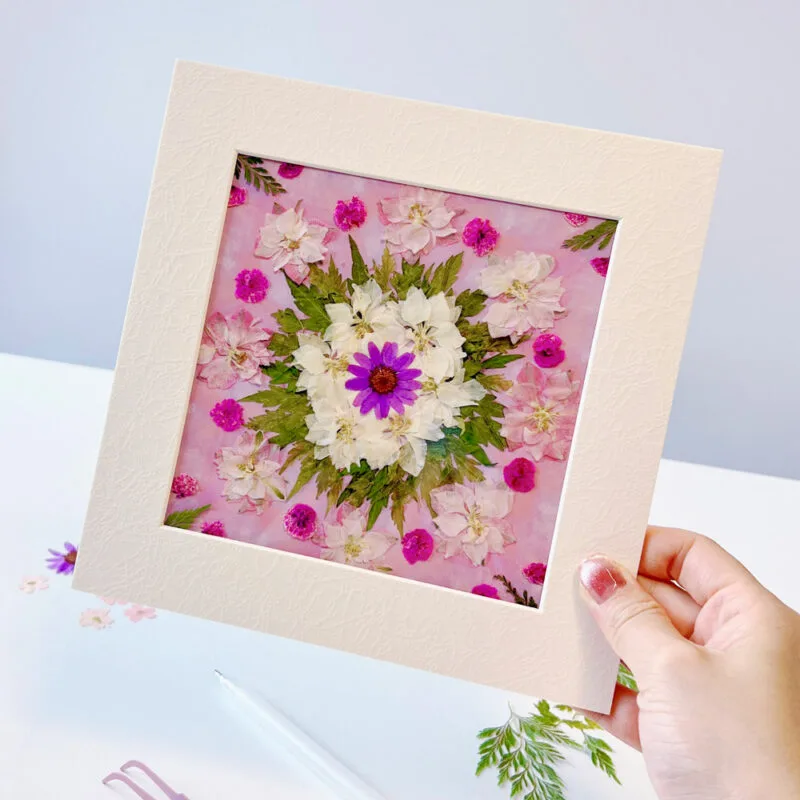 Hand holding framed pressed flower mandala made with seasonal pressed flower materials
