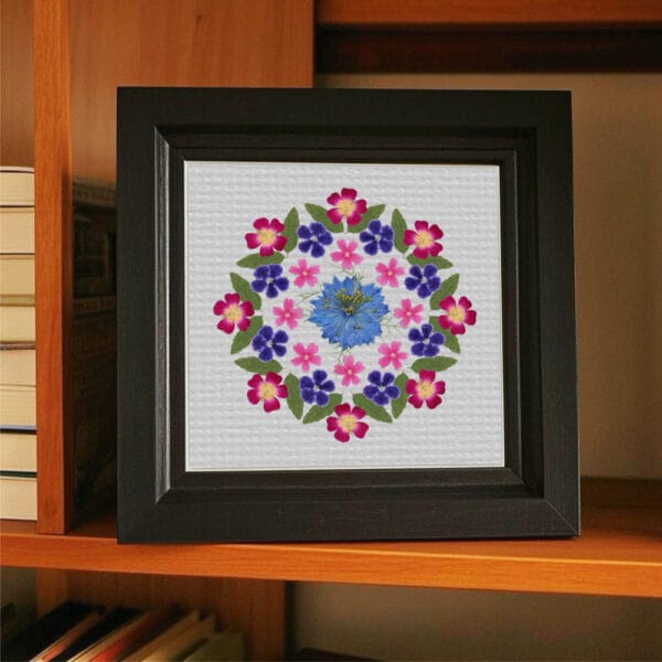 Finished pressed flower mandala framed on a bookshelf, created with petal & still beginner kit