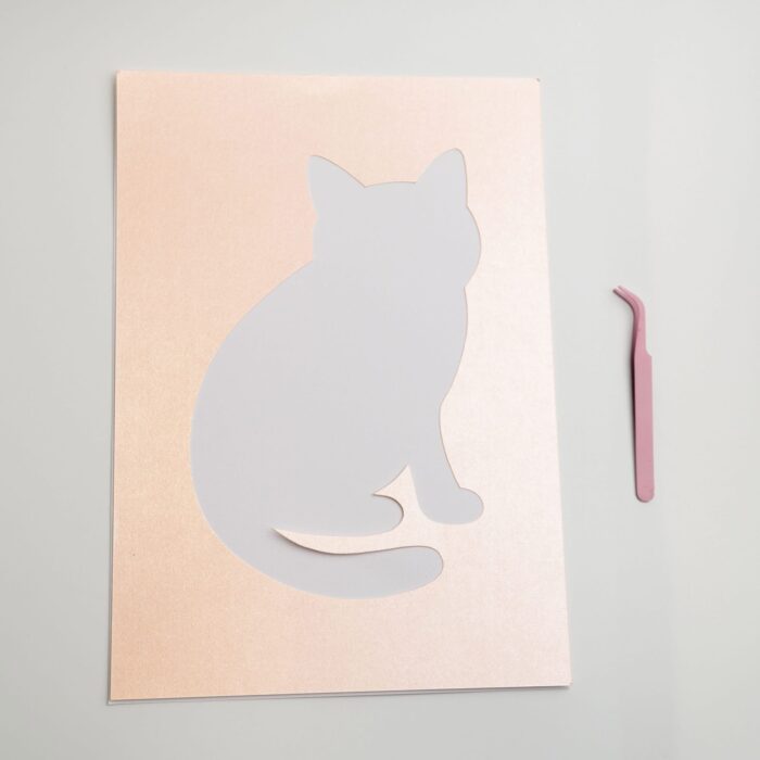 Close-up of the cat-shaped cutout template on shimmer peach-toned paper, included in the curious pressed flower kit.