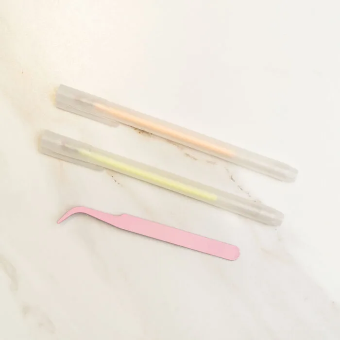 Pressed flower kit tools featuring a pink angled tweezers and two pastel gel pens, used for delicate arrangement of pressed flowers.