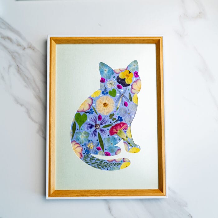 Pressed flower cat design featuring soft blue, yellow, and pink blooms on a pale green background.