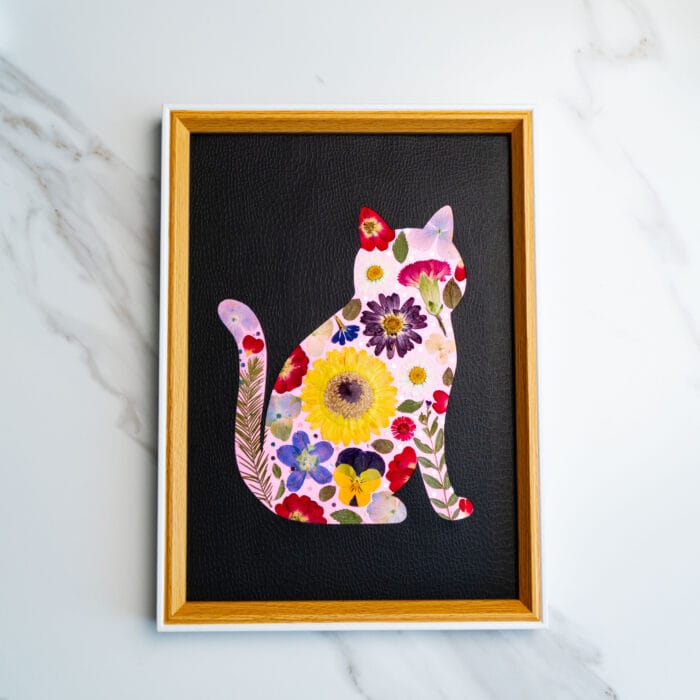 Bright yellow sunflower-themed pressed flower cat silhouette on a rich black leather-textured background.
