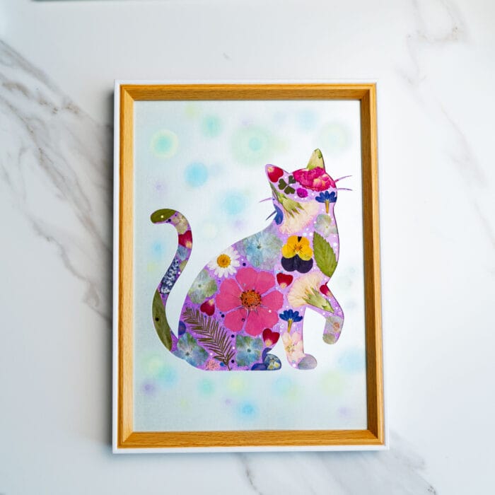 Playful pressed flower cat looking upward, filled with colorful pink and purple blooms on a dotted pastel background.