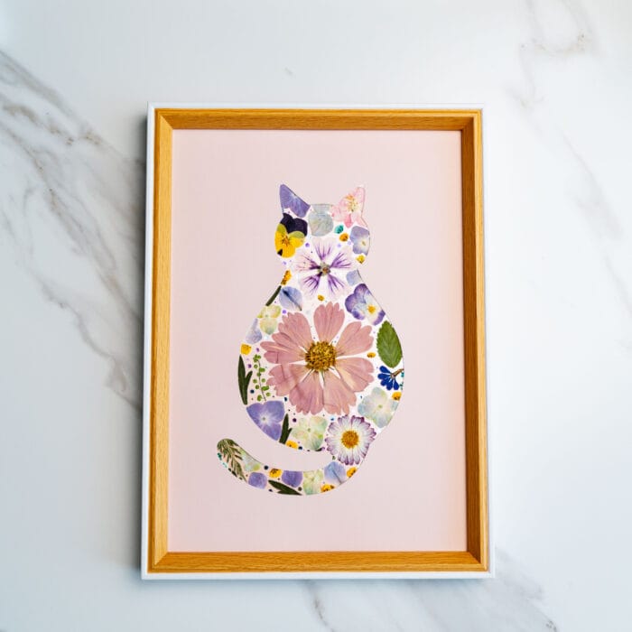 Pressed flower cat silhouette with soft pastel blooms and a large pink daisy, set on a gentle blush background.