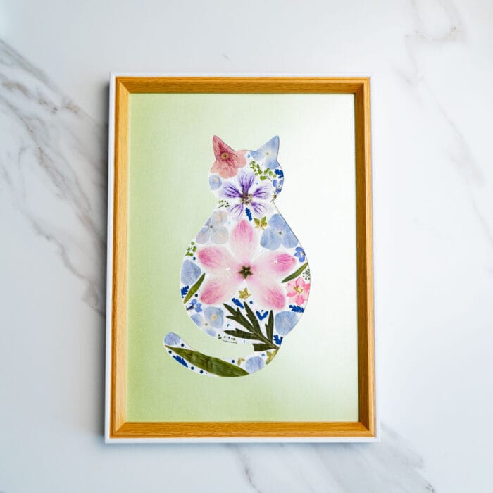 Gentle pressed flower cat featuring soft pink and blue tones on a light green background.