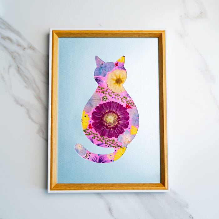 Pressed flower cat with large purple and yellow flowers, set against a cool blue background.
