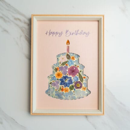 Pressed flower art of a birthday cake silhouette with blue and purple flowers, decorated with a candle on a pink background