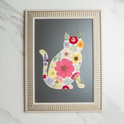 Pressed flower art of a cat silhouette decorated with colorful flowers on a black background