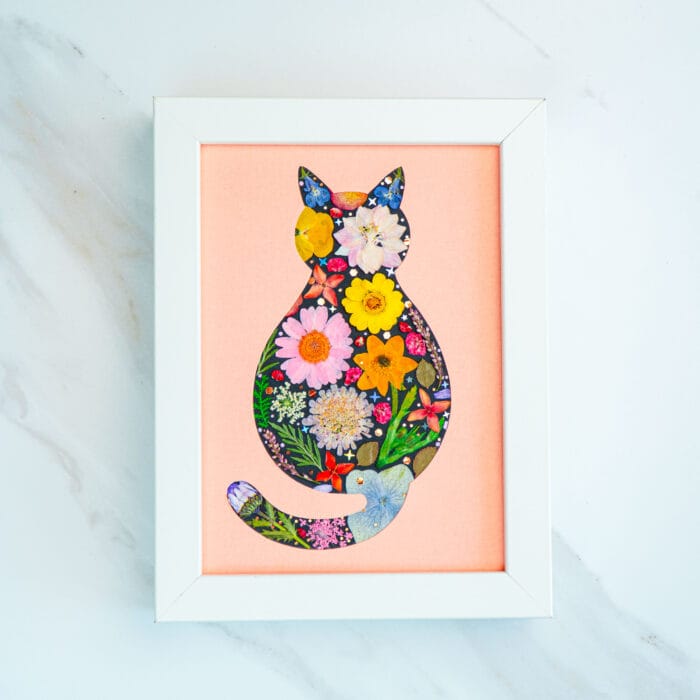 Pressed flower cat artwork against soft pink background, blossom-filled silhouette of a sitting cat