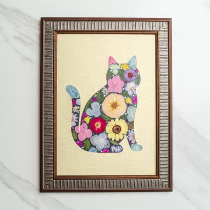 Pressed flower art of a cat silhouette filled with pink, yellow, and blue flowers on a golden background