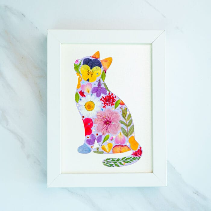Pressed flower cat artwork full of vibrant purple, pink and yellow blooms, joyful handmade floral collage