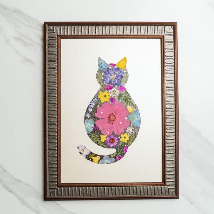 Pressed flower art of a cat silhouette with a large pink flower in the center, decorated with colorful blossoms