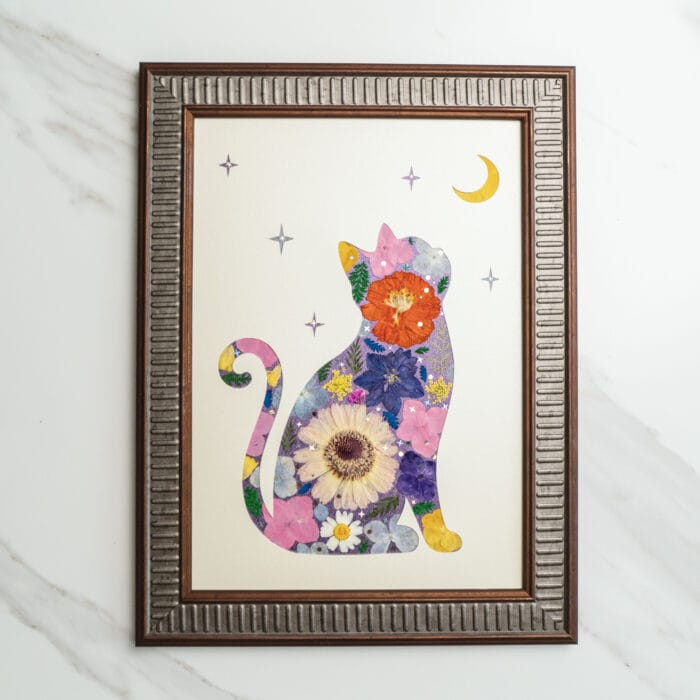 Pressed flower art of a cat silhouette filled with vibrant flowers, gazing at the crescent moon and stars