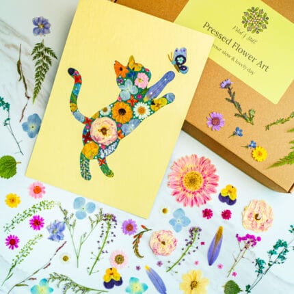 Pressed flower cat artwork of a playful cat reaching for a butterfly, colorful handmade floral collage with flowers around
