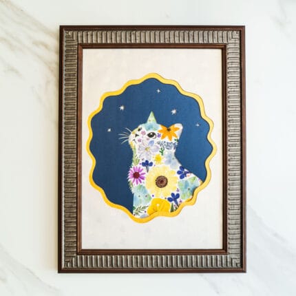 Pressed flower art of a cat silhouette looking up at stars, decorated with bright flowers and framed with a dark blue background