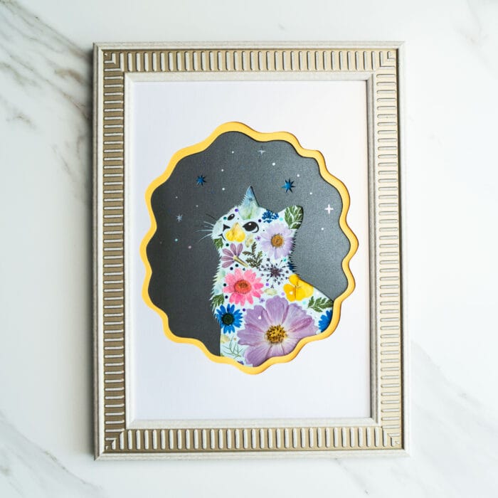 Pressed flower art of a cat silhouette with pink and yellow flowers on a starry black background