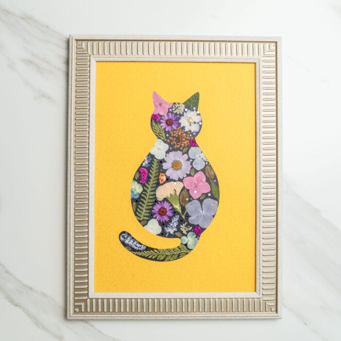 Pressed flower art of a cat silhouette filled with colorful flowers on a bright yellow background