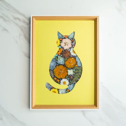 Pressed flower art of a cat silhouette with orange and blue flowers on a yellow background