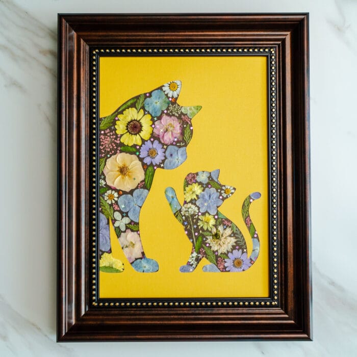 Pressed flower art of a mother cat and kitten silhouette with colorful flowers on a yellow background