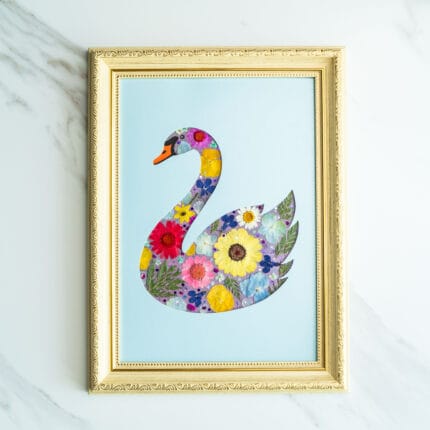 Pressed flower art of a swan silhouette filled with colorful flowers on a blue background