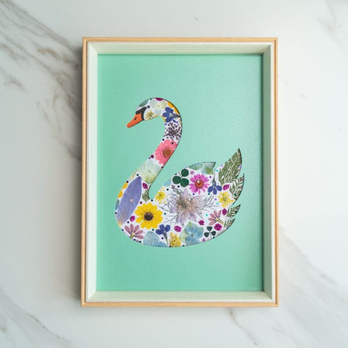 Pressed flower art of a swan silhouette filled with flowers on a green background