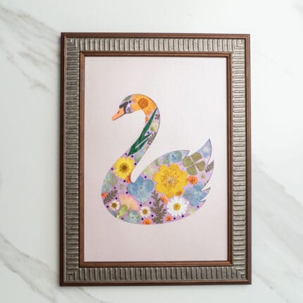 Pressed flower art of a swan silhouette decorated with yellow and purple flowers on a soft pink background