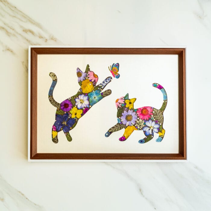 Pressed flower art of two cats made of flowers playing with a butterfly