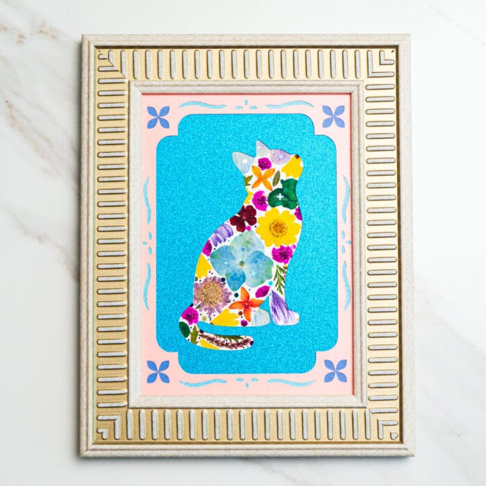Pressed flower cat collage in bright blooms, framed with pink and blue accents on a silver frame.