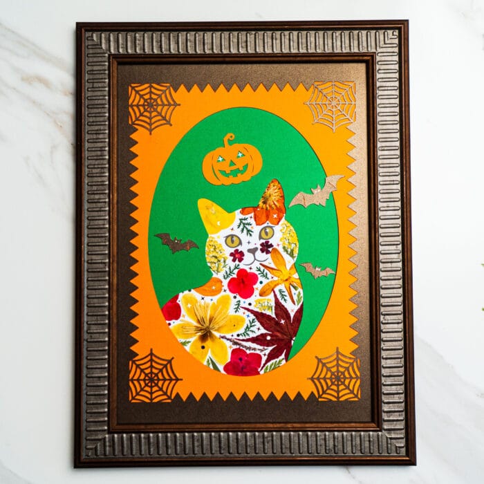 Halloween pressed flower cat with pumpkins, bats, and spider web accents, framed in bronze.