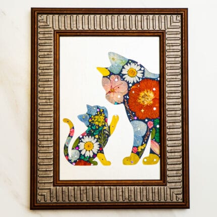 Pressed flower art showing a mother cat and kitten silhouette filled with colorful petals, in a bronze frame.