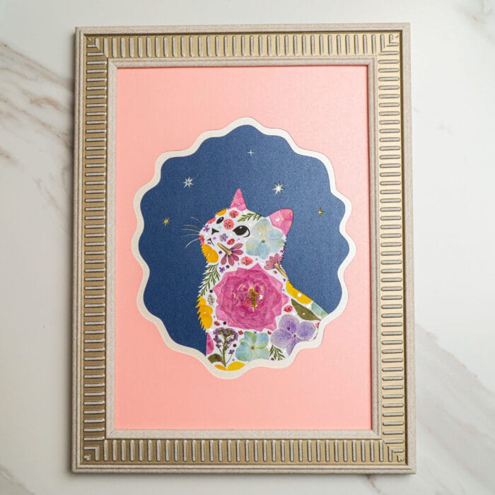 Pressed flower cat artwork with colorful floral patterns, framed against a navy starry background and pink border, finished piece in decorative frame.