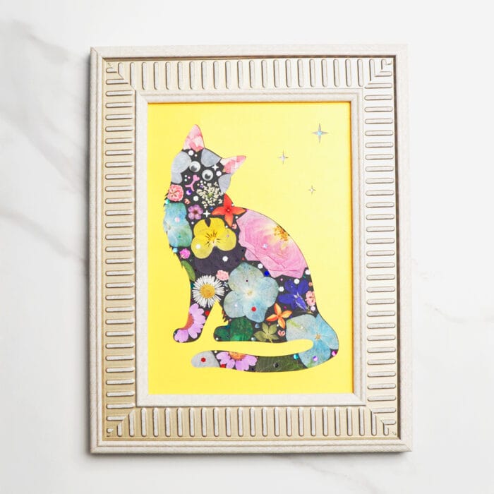 Pressed flower cat silhouette with colorful blossoms on dark base, wearing a red bow, set against a bright yellow background with stars, framed in light gold frame.