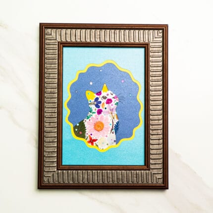 Pressed flower cat silhouette decorated with vibrant blossoms, set against a blue background with yellow scalloped border.