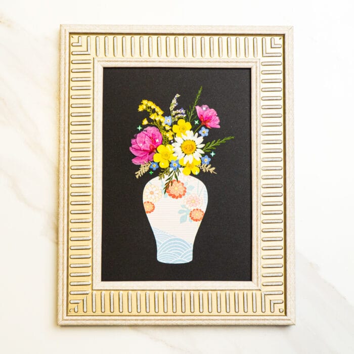 Pressed flower bouquet in a patterned vase on black background, framed in silver.