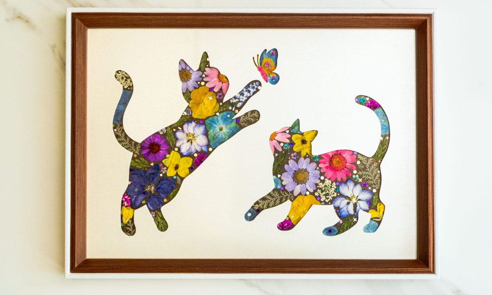 Pressed flower art of two cats made of flowers playing with a butterfly
